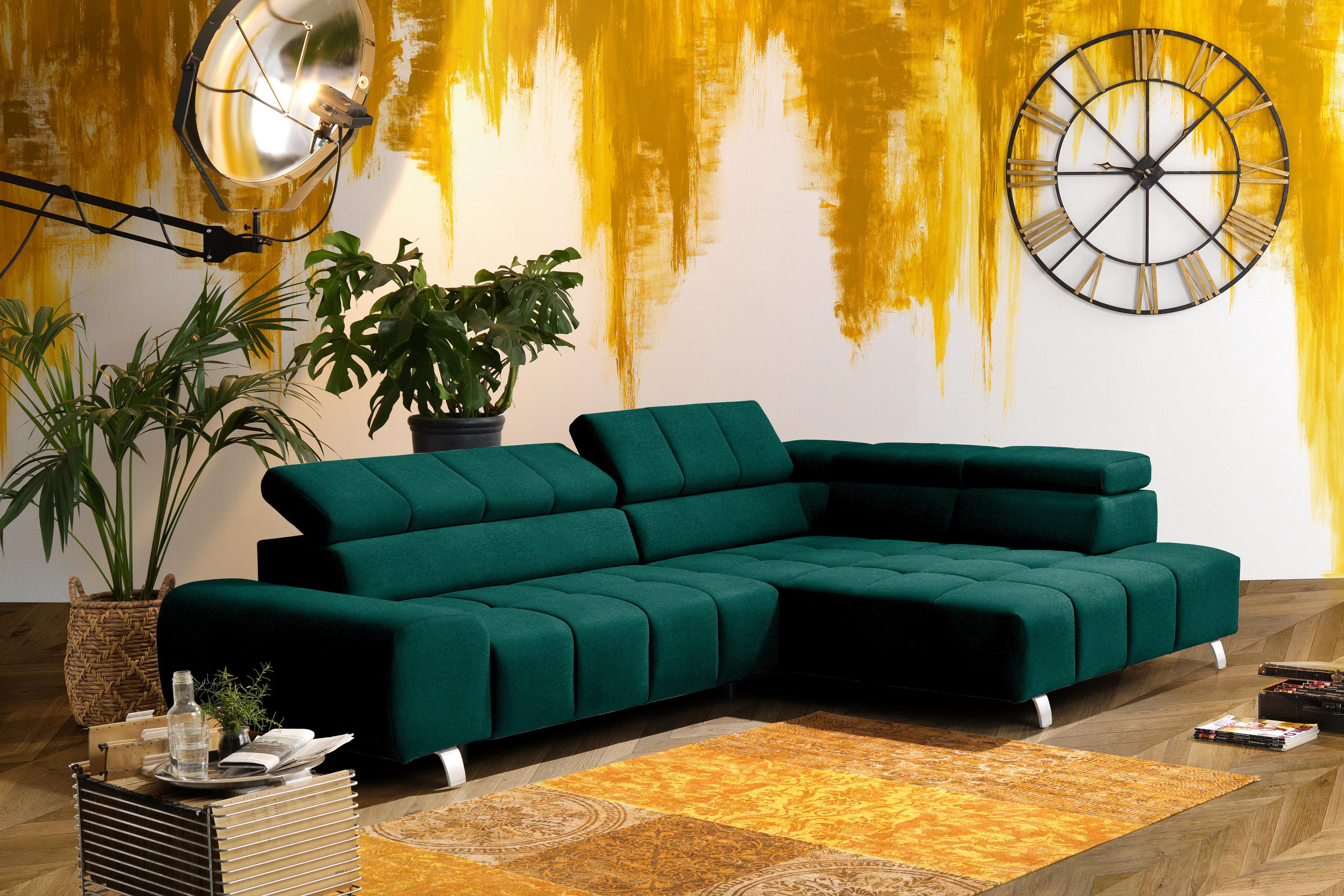 Hom`in ECKSOFA Grün Webstoff, links davon: Topfpflanze in grün, Beistelltisch, rechts davon: Webteppich in orange, Deckenbeleuchtung in hellem Wohnzimmer.