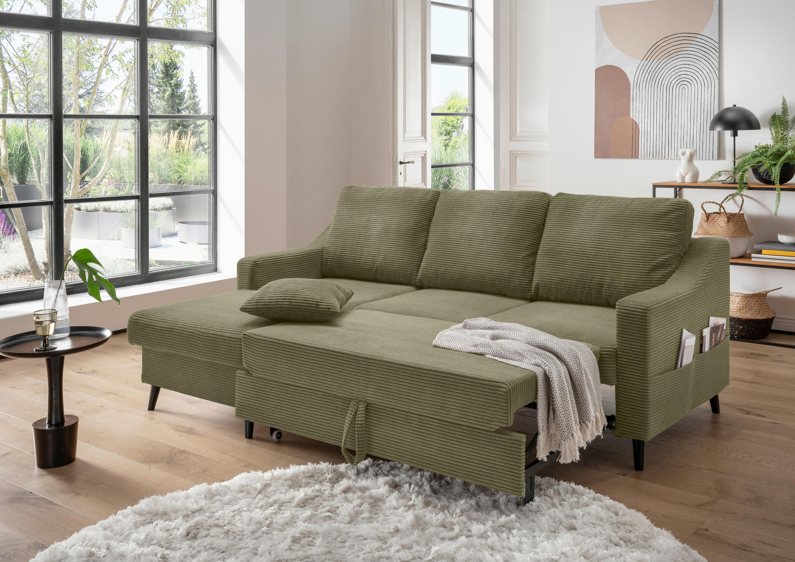 P & B ECKSOFA Olivgrün Cord, links davon: Kunstfell in weiß, Beistelltisch in braun, rechts davon: Decke, Lektüre in hellem Wohnzimmer.