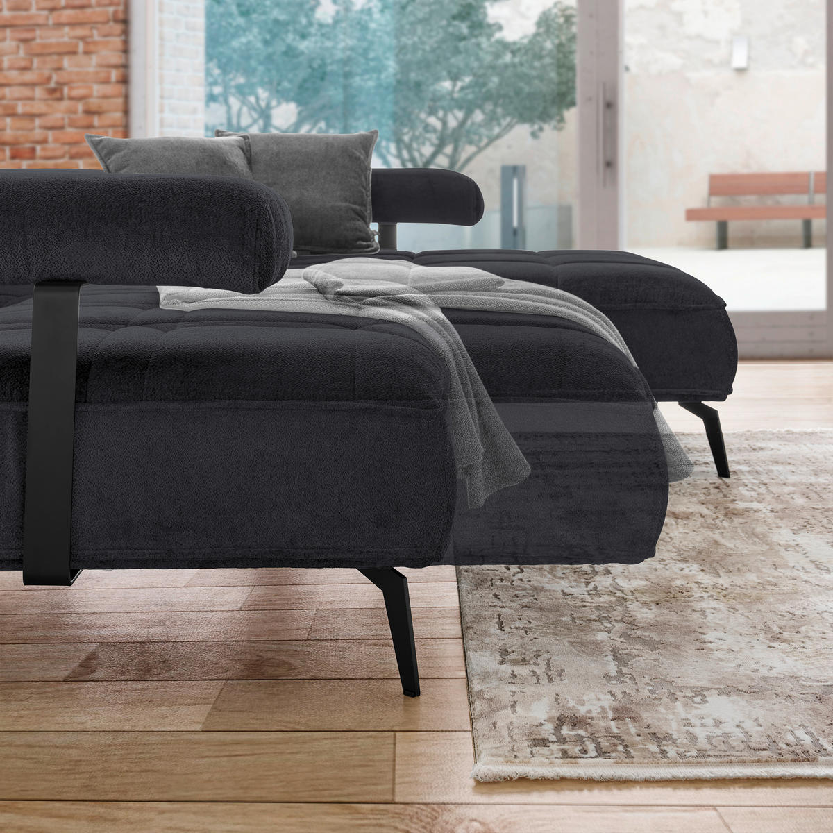 Welnova ECKSOFA Schwarz Webstoff, links davon: Kissen in grau, rechts davon: Decke in grau, Kunstfell in hellem Wohnzimmer.