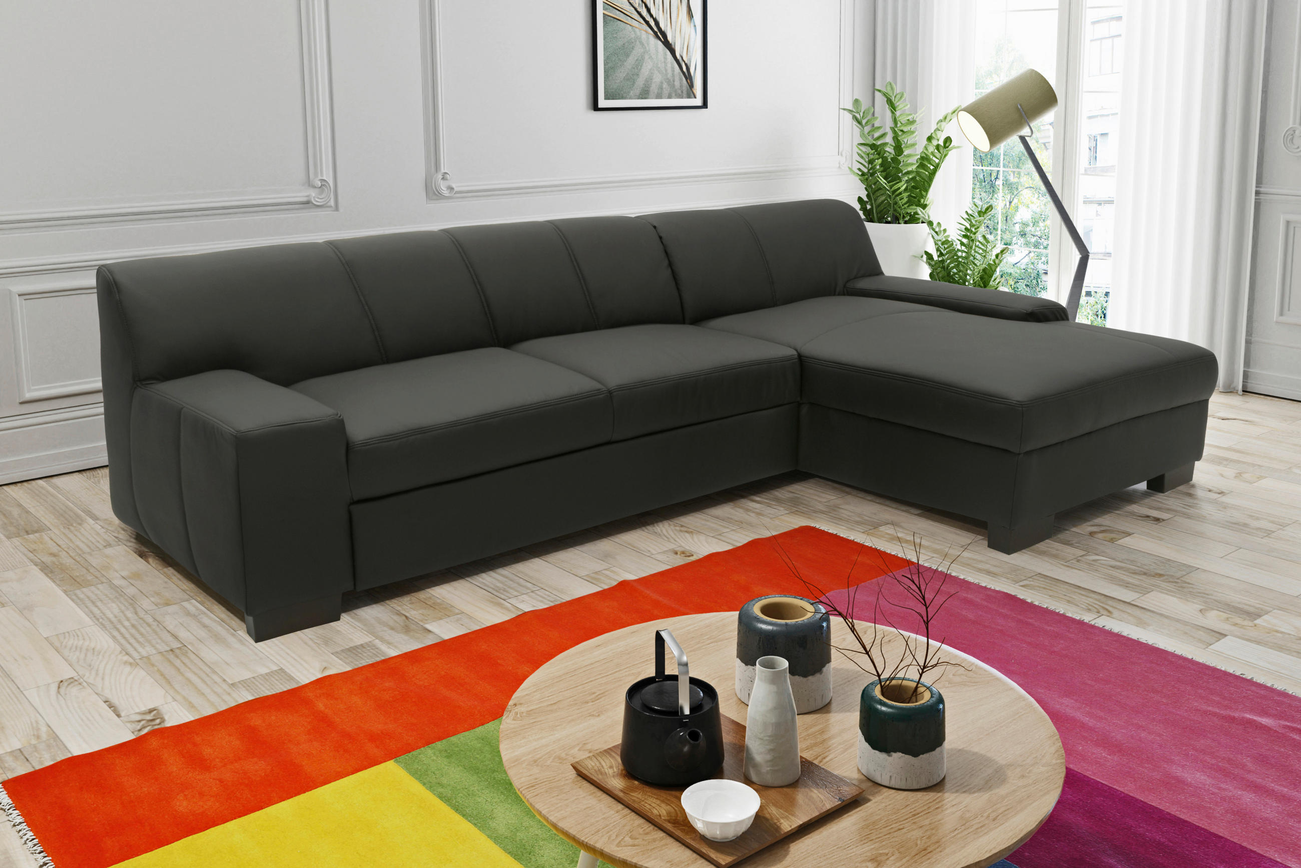 MID.YOU ECKSOFA Schwarz Lederlook, rechts davon: Hochflorteppich, Store in weiß, Topfpflanze in grün, Bild in hellem Wohnzimmer.