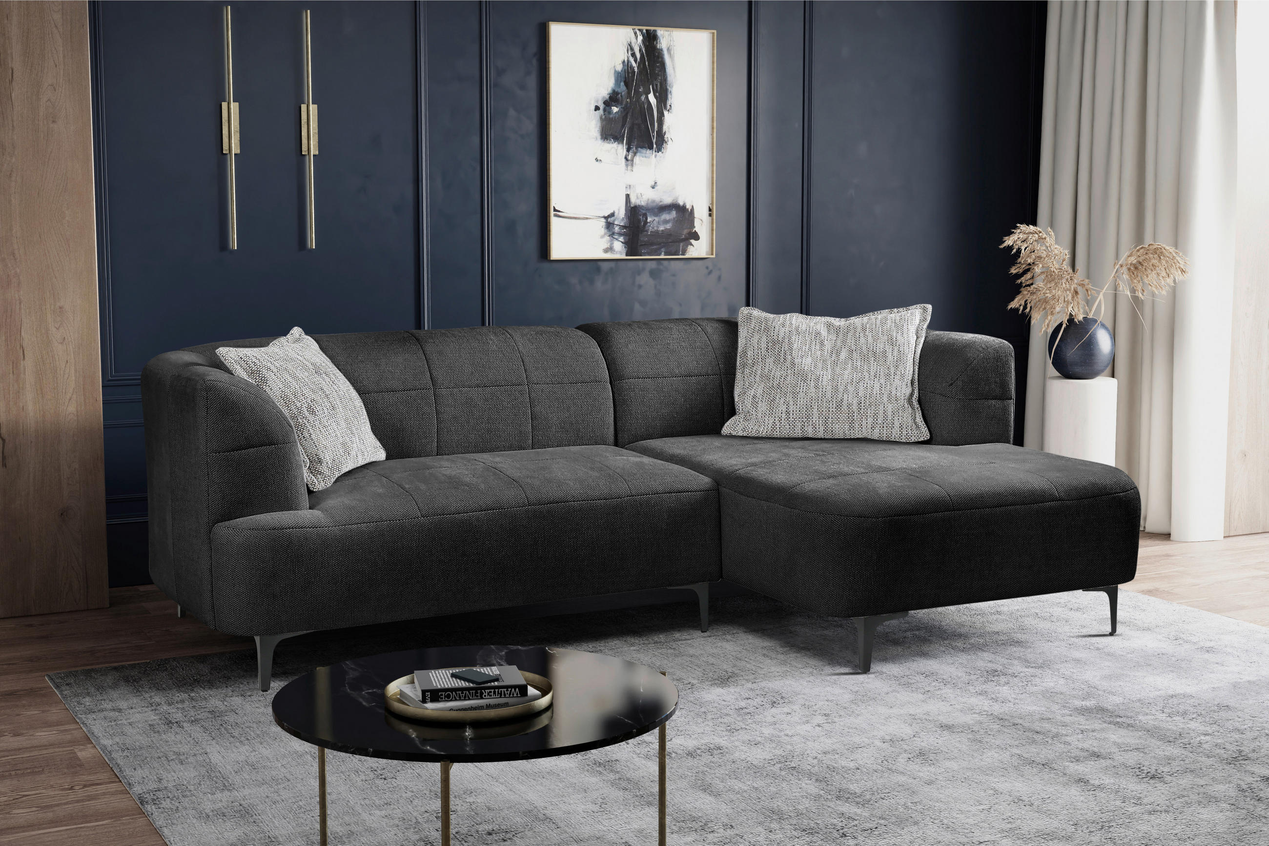 MID.YOU ECKSOFA Dunkelgrün Struktur, links davon: Hochflorteppich in schwarz, Beistelltisch in schwarz, Kissen in weiß, rechts davon: Gardine in dunklem Wohnzimmer.