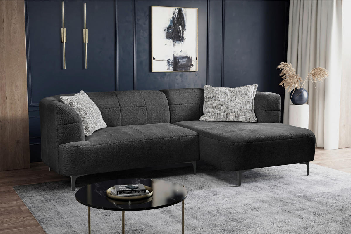 MID.YOU ECKSOFA Dunkelgrün Struktur, links davon: Hochflorteppich in schwarz, Beistelltisch in schwarz, Kissen in weiß, rechts davon: Gardine in dunklem Wohnzimmer.