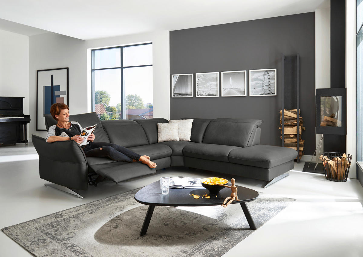 Hukla ECKSOFA inkl. Funktionen Valdera Schwarz Echtleder, rechts davon: Hochflorteppich, Couchtisch, Kissen in weiß, Kamin in hellem Wohnzimmer.