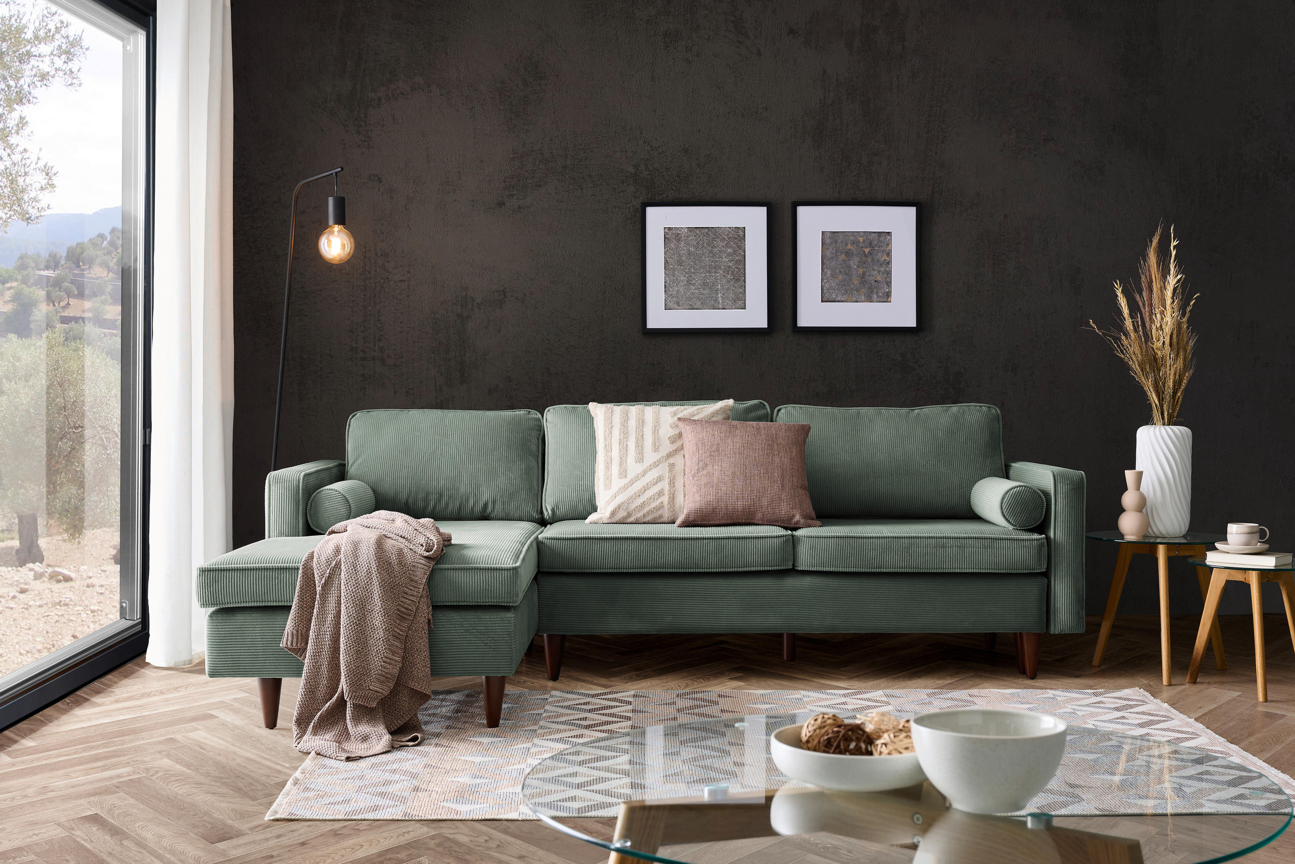 Livetastic ECKSOFA Grün Cord, links davon: Decke, rechts davon: Webteppich in weiß, Kissen in grün, Schale in dunklem Wohnzimmer.