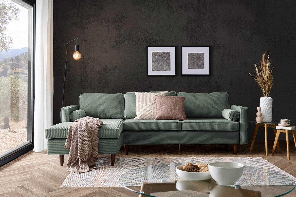 Livetastic ECKSOFA Grün Cord, links davon: Decke, rechts davon: Webteppich in weiß, Kissen in grün, Schale in dunklem Wohnzimmer.