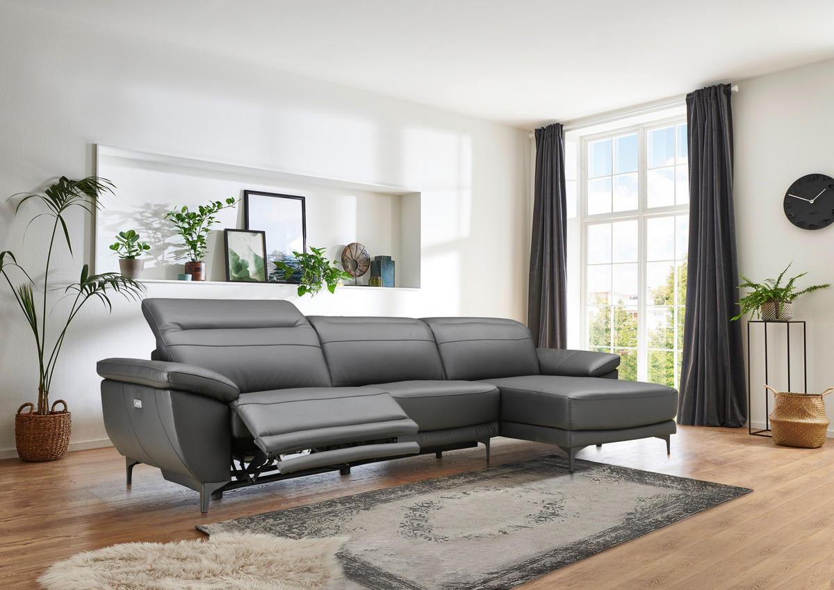 Xora ECKSOFA inkl. Funktionen Ronald Schwarz Echtleder, Kombination Echtleder/Lederlook Lederlook, links davon: Hochflorteppich, rechts davon: Blume in grün, Gardine, Beistelltisch in hellem Wohnzimmer.