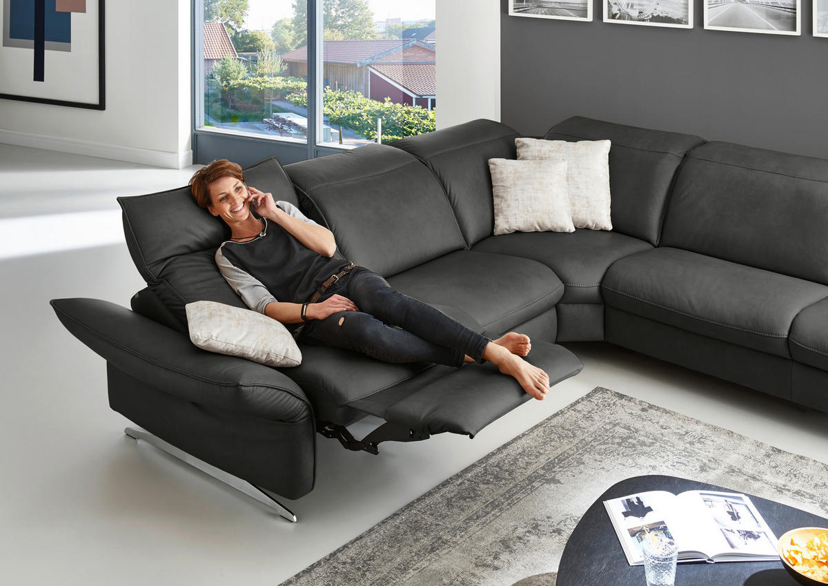 Hukla ECKSOFA inkl. Funktionen Valdera Schwarz Echtleder, links davon: Bild, rechts davon: Hochflorteppich, Lektüre in weiß, Kissen in weiß in dunklem Wohnzimmer.