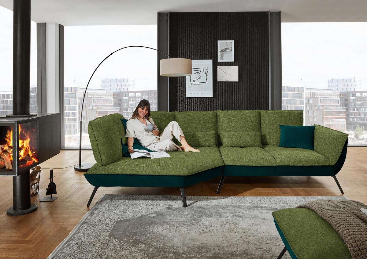 Moderano ECKSOFA Grün Flachgewebe, links davon: Hochflorteppich, rechts davon: Stuhl in grün, Kissen in grün, Bild in weiß in hellem Wohnzimmer.