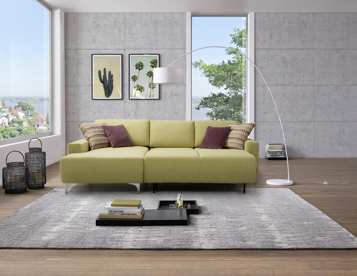 Sedda ECKSOFA Hellgrün Chenille, links davon: Hochflorteppich in grau, Lektüre, rechts davon: Kissen, Bild in hellem Wohnzimmer.