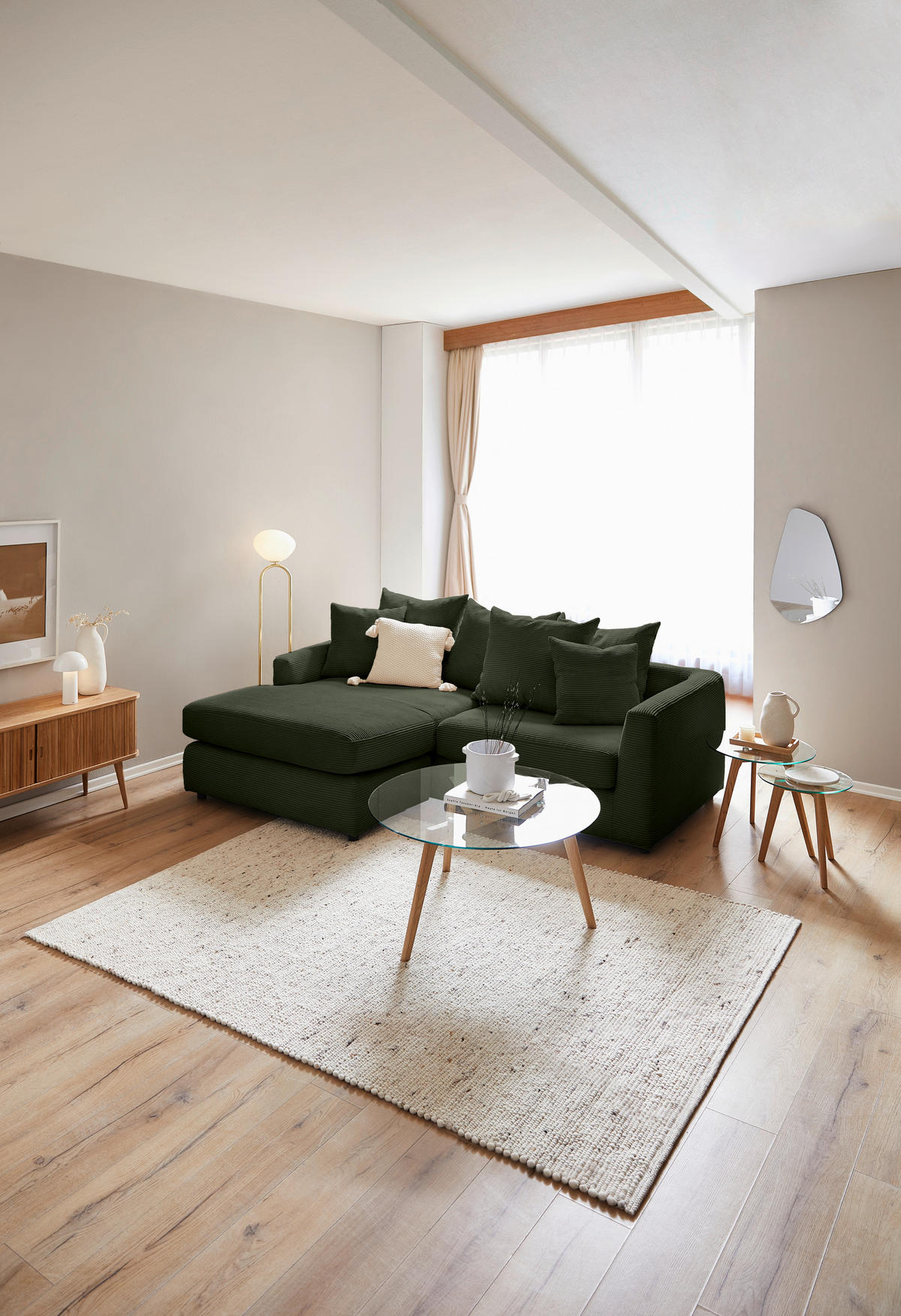home24 ECKSOFA Dunkelgrün Cord, links davon: Hochflorteppich, Sofa in grün, rechts davon: Lektüre, Beistelltisch in hellem Wohnzimmer.